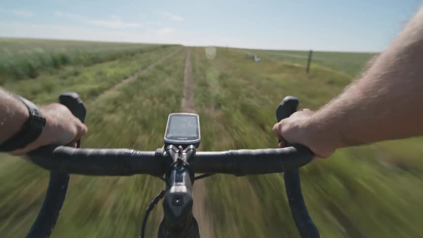 Cyclist rides bicycle on country road near fields seen through point of view