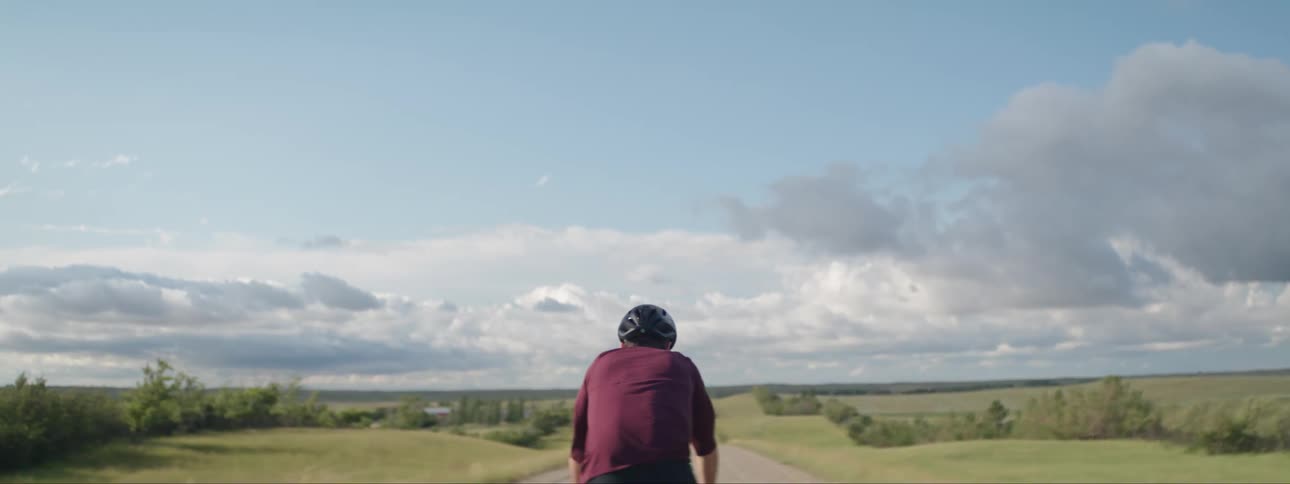 Male cyclist with helmet red sweatshirt pedals along dirt road in the countryside