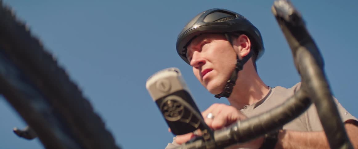 A man wearing a helmet stands over his bicycle as he looks confused about which direction to take