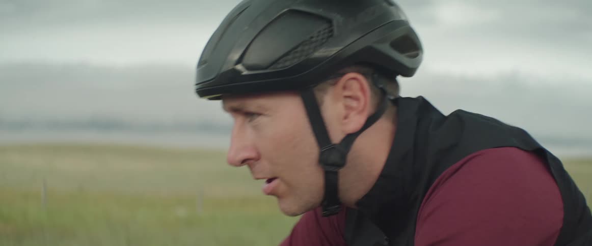 Focused man wearing a cycling helmet riding his bike in the road in a stormy rural area