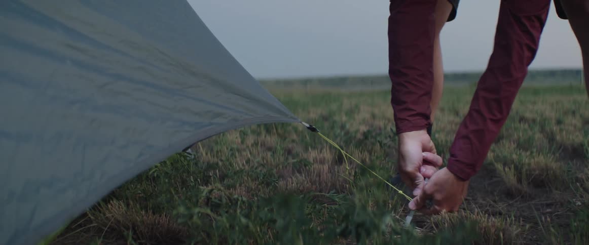 Person sets tent stake while setting up camp