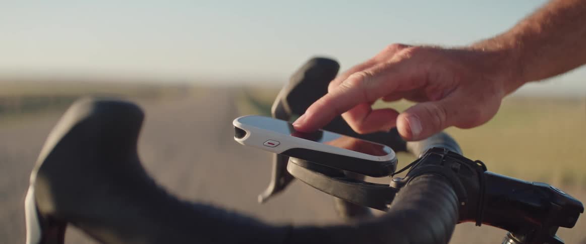 Male cyclists scrolls and makes selections on mobile device attached to bicycle handlebars while standing near road in countryside