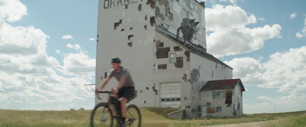 Cyclist pedals along road passing an abandoned grain elevator