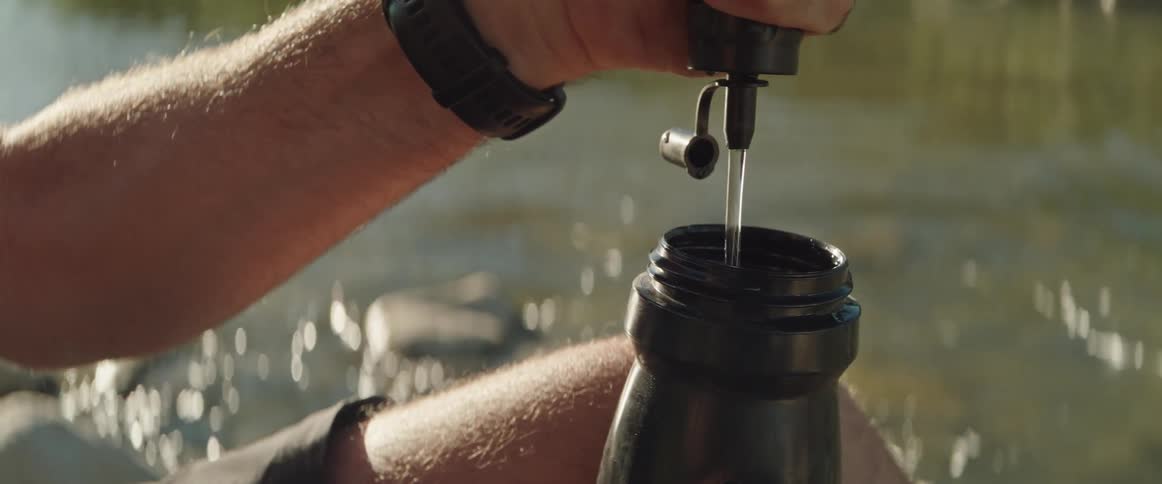 A man is filtering water from a river and pouring it into a bottle