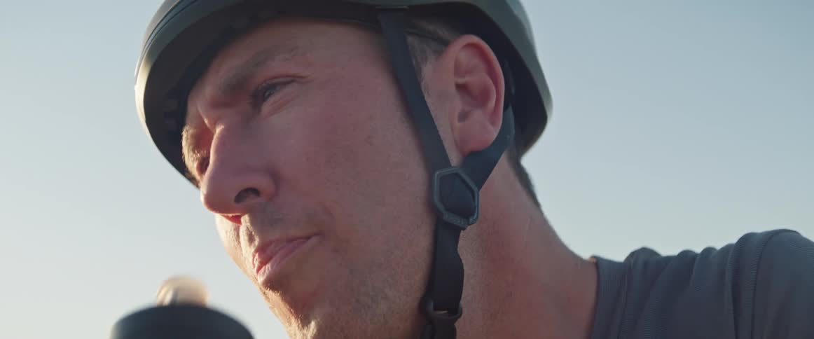 Man wearing a bicycle helmet drinks water from a bottle in the evening