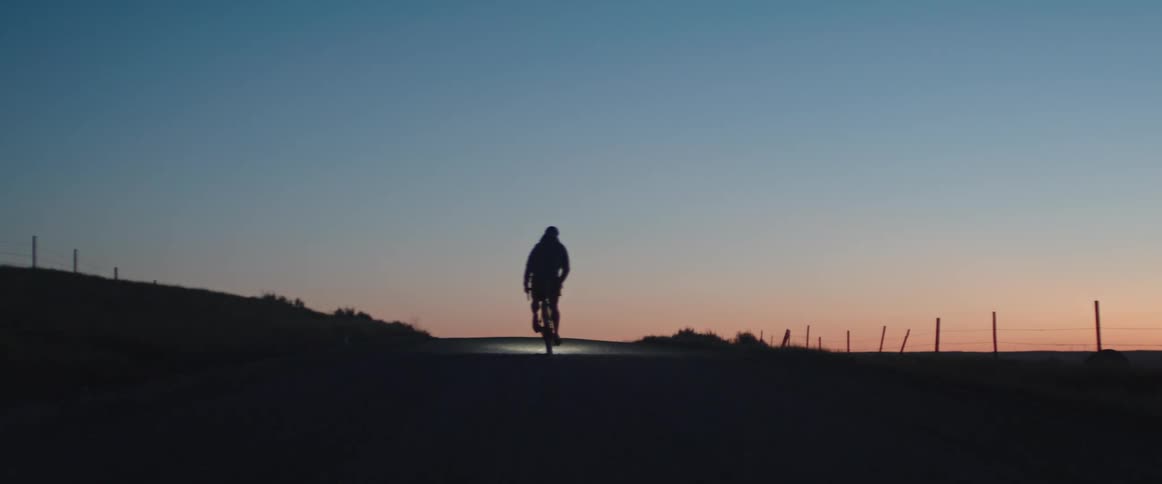 Male cyclist cresting a hill is silhouetted against the sky at dusk