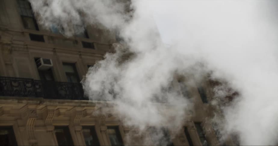 Steam billows from a building in he midst of an urban environment filled with tall buildings