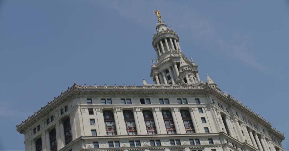 Architecturally detailed building with tower topped by a gold statues stands near church