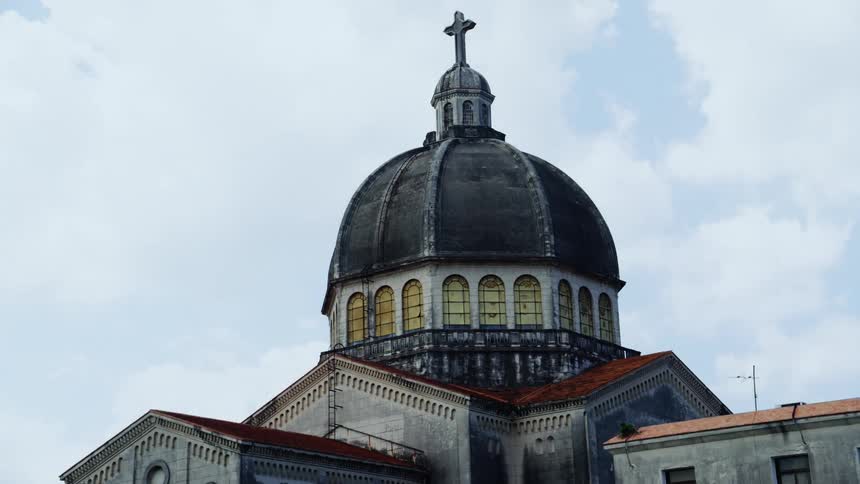 Large stone cross sits on dome of large church under a heavily clouded sky