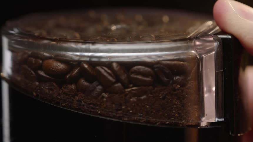 A person has their finger on a container of coffee beans