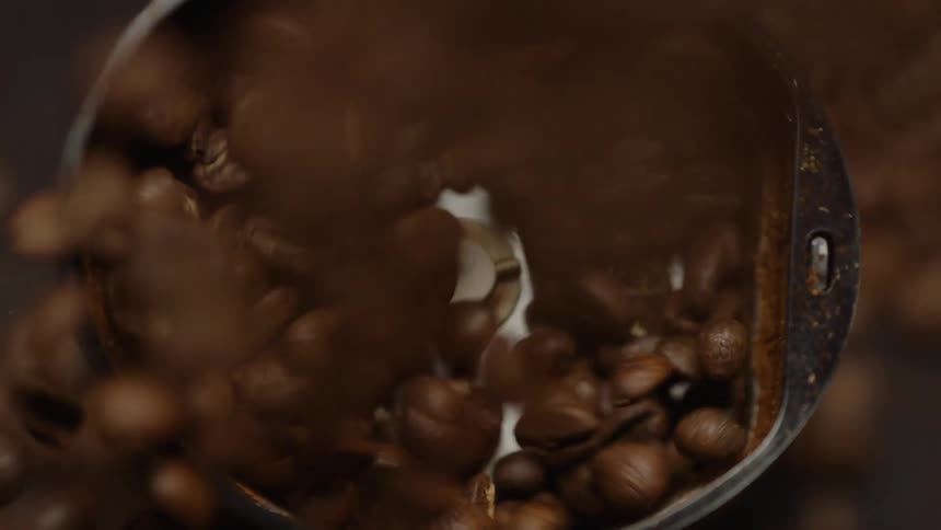 A small coffee grinder has a pile of coffee beans poured into it to be ground