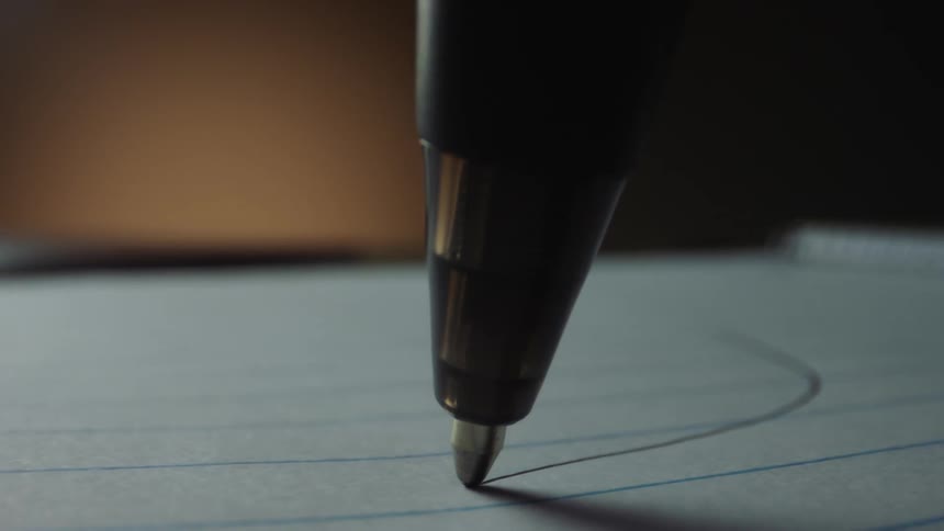 Extreme close up of the tip of a pen drawing a line with ink over paper