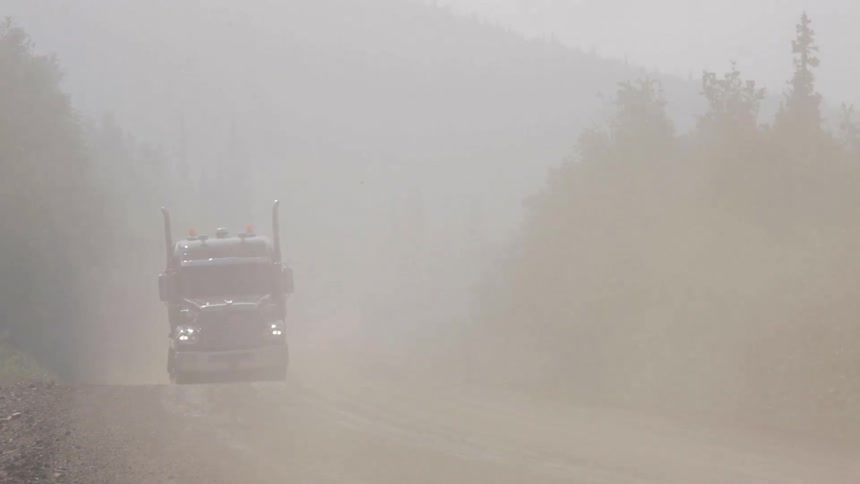 Trucks driving down a dusty road