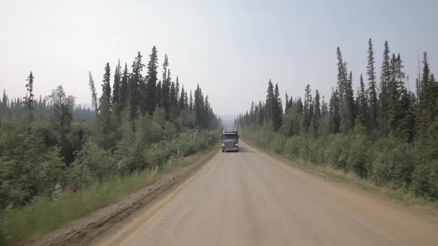 A truck is traveling down a dirt road by a forest