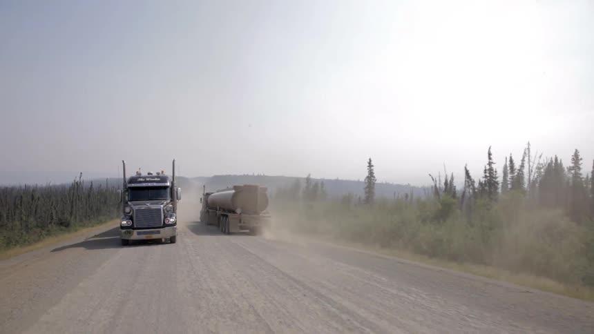 Two semi trucks passing each other on a dusty flat road