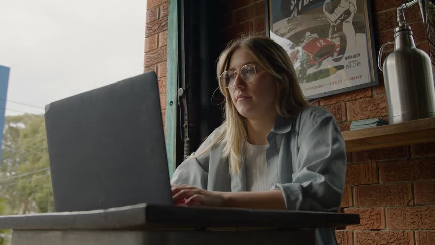 A woman is sitting in front a laptop computer and she opens the lid and types on the keyboard