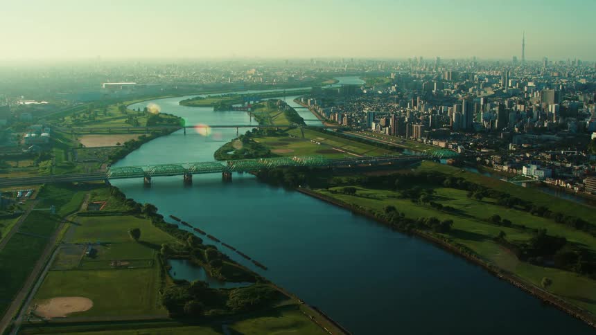 Traffic moves across a bridge crossing a river outside a big city with tall buildings and skyscrapers in a hazy sky
