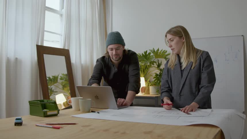 Colleagues discuss blueprints while scrolling through a laptop