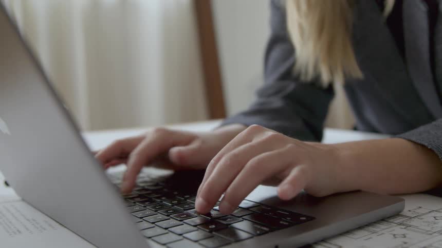 A woman sits at a table where she types very rapidly on her laptop keyboard