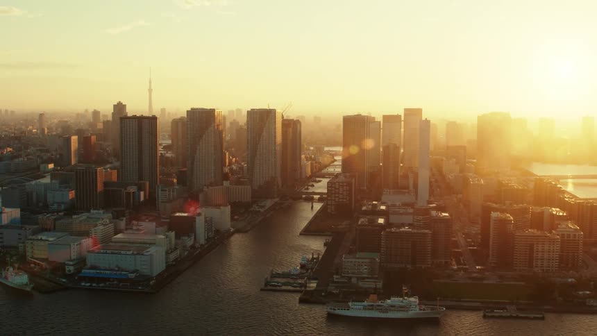 The sun shines brightly upon a city on the coast with boats in the water and tall buildings on the city skyline