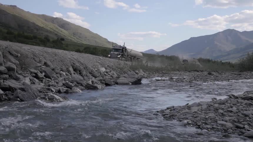 Trucks speed along a road next to a flowing river