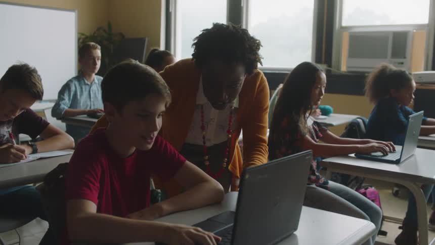A school teacher instructs a student using a laptop