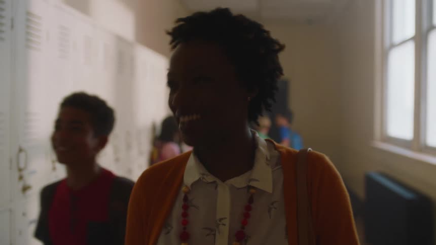 A teacher smiles as she walks down the hall and greets students