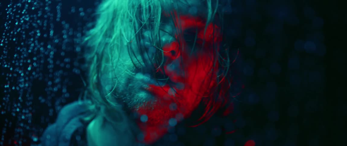 A man frosts up the glass while standing with his eyes closed behind a rain drenched window