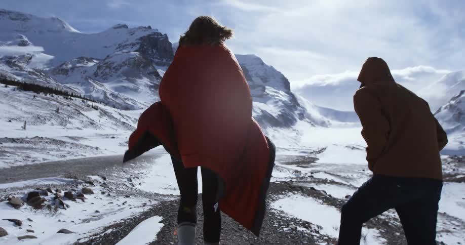 A man and woman are walking outside near snow covered mountains