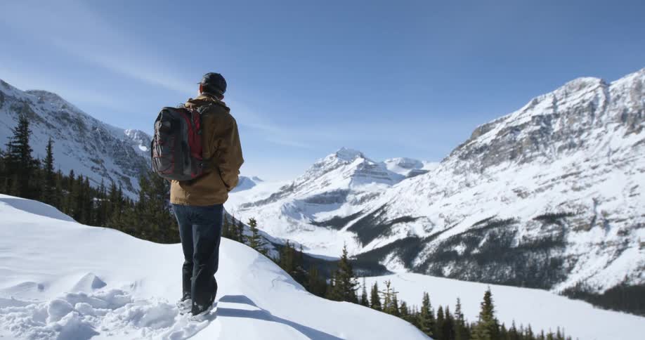 A man wearing a backpack stands in snow by a cliff