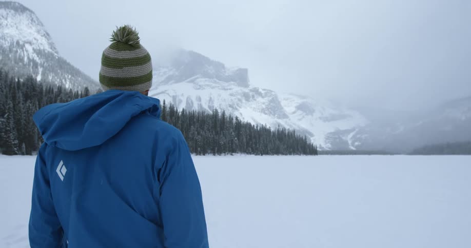 A man looks out towards mountains and pine trees during a snowstorm