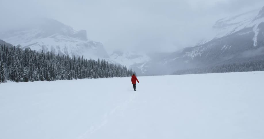 A person walks alone through a snowy field in the mountains