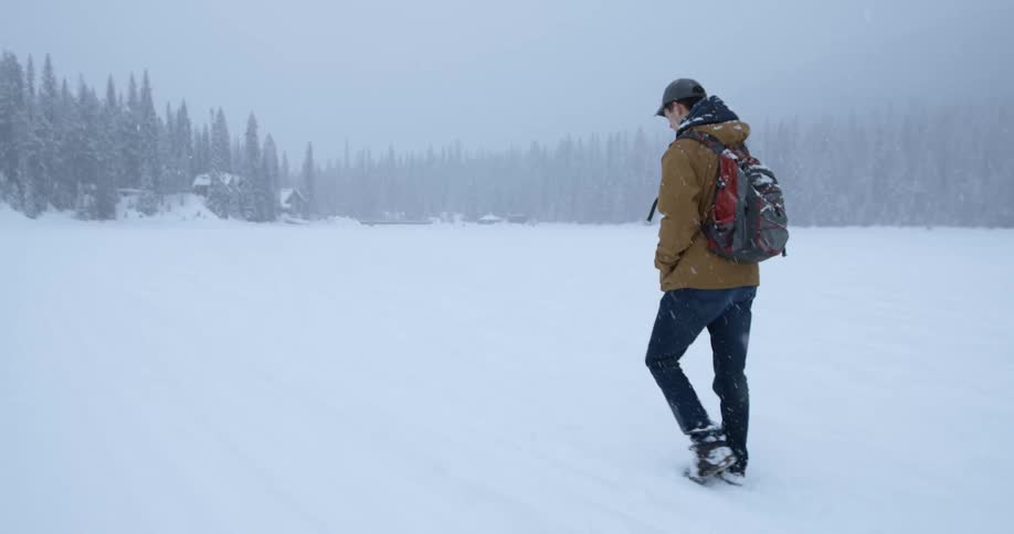 A man is walking across a snow covered field as it snows heavily