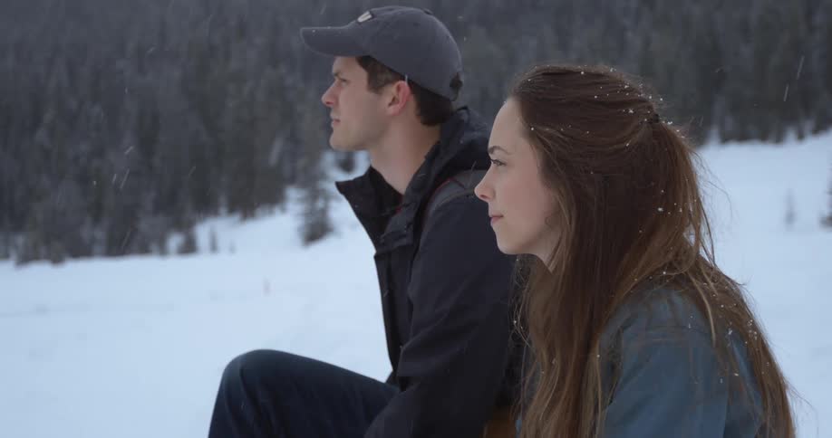 A man and woman sitting outside talking while it snows