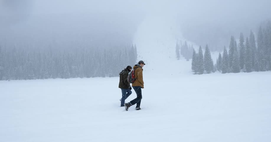 Two hikers walk across a field in the wilderness during a snowstorm
