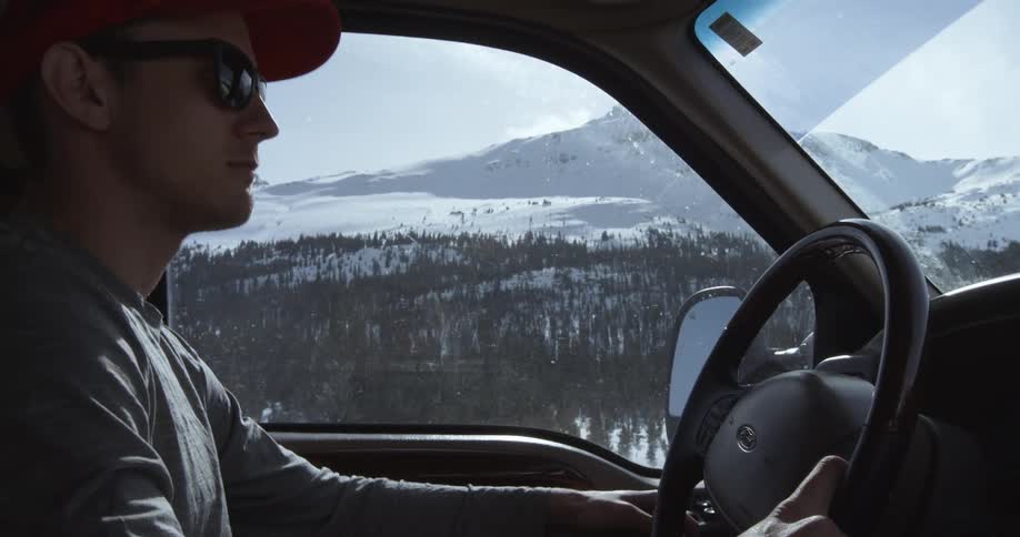 Man driving through a snowy wilderness wearing sunglasses on an overcast day