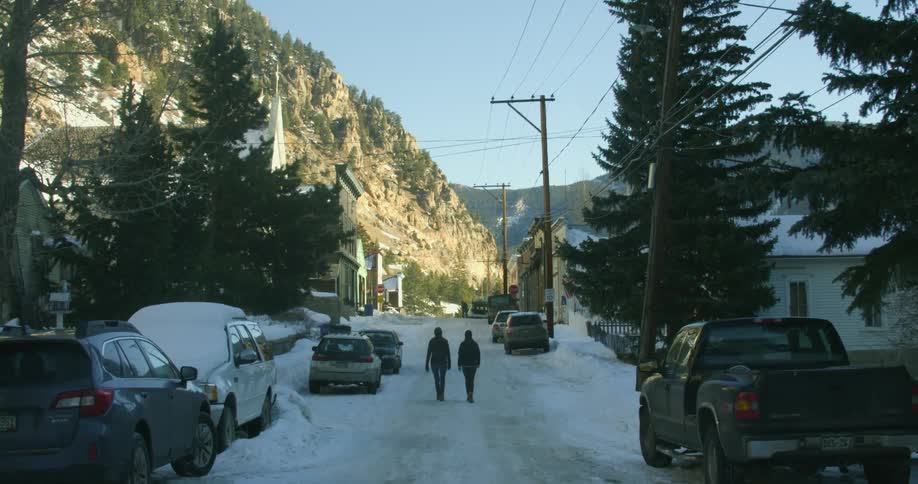 Two people walk down a road with a hill in the distance
