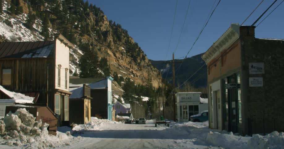 Small buildings are nestled at the base of snowy mountains