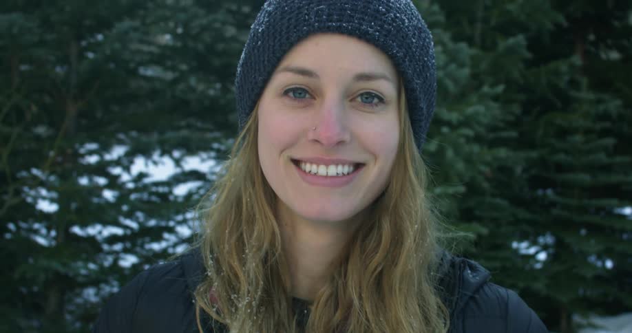 A woman smiles standing in front of some trees
