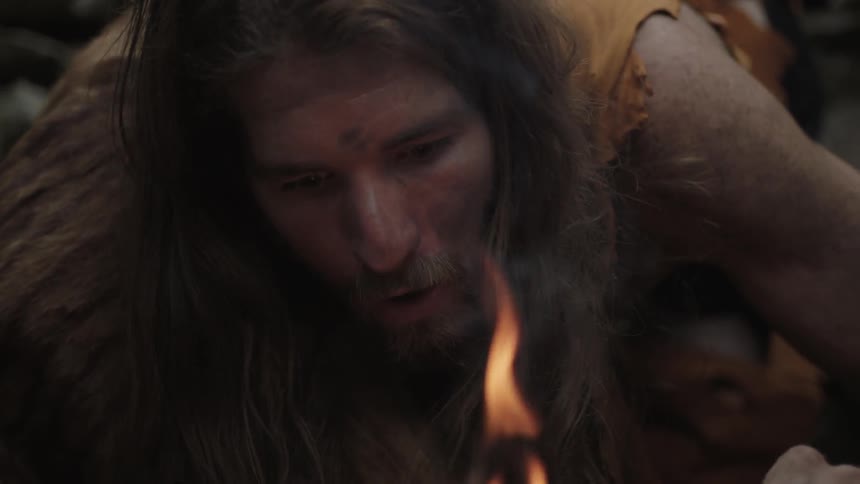 A man piles sticks onto a small fire