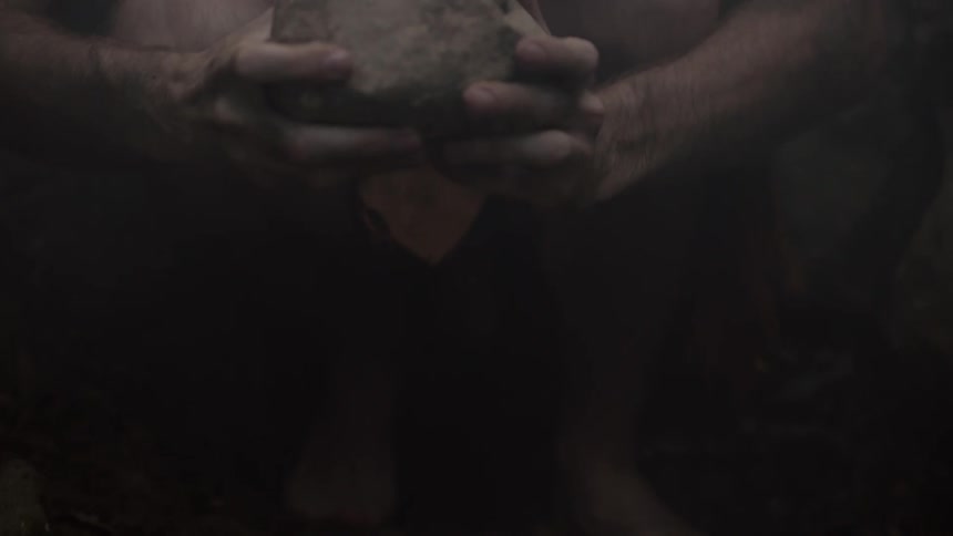A man picking up a large rock and raising it over his head