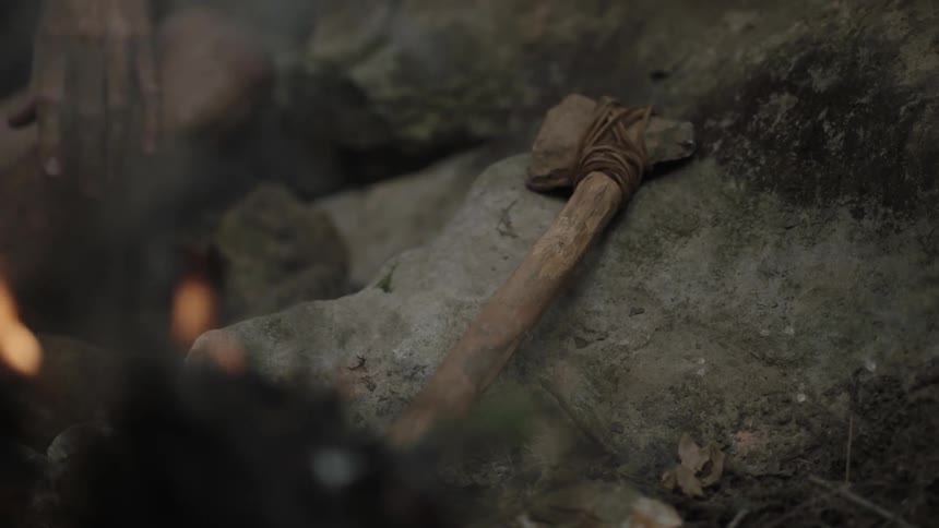 A person is crouched by a campfire with an axe nearby
