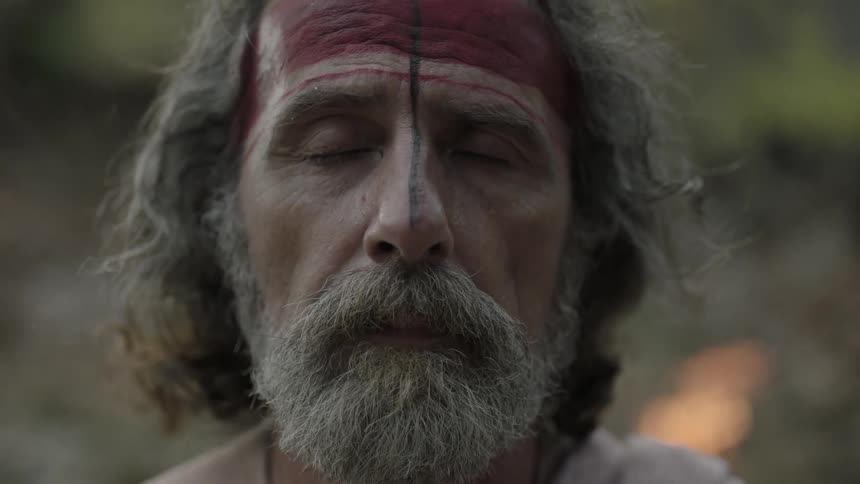 A man with paint on his face closes his eyes and looks up