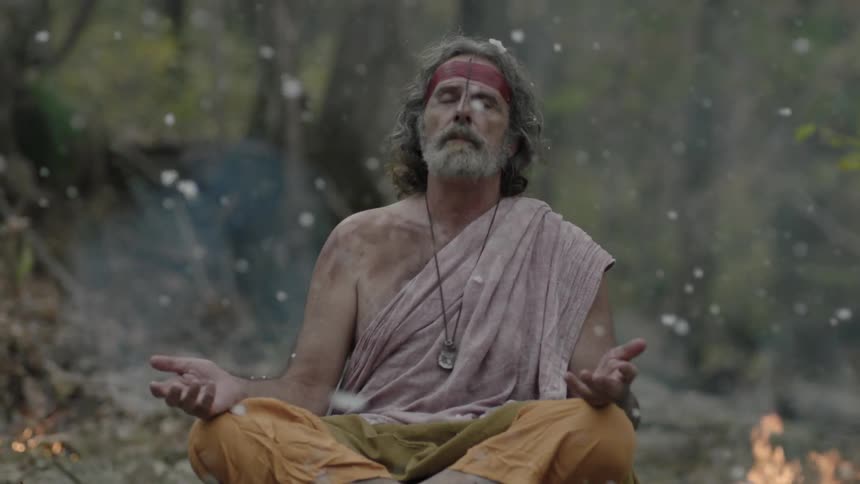 A man sits in a forest while ash falls on him