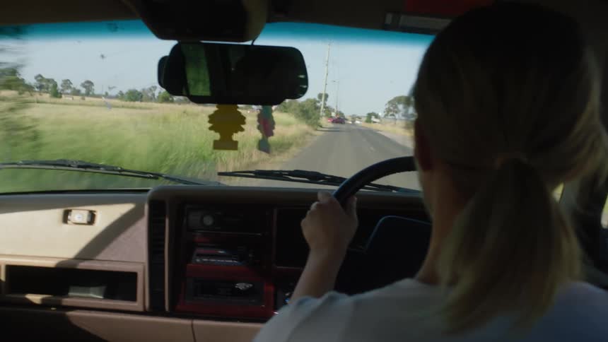 A woman driving a jeep down a rural road with the steering wheel on the right hand side