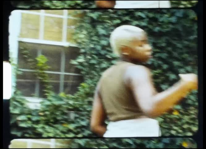 A woman is standing outside near trees and a building dancing