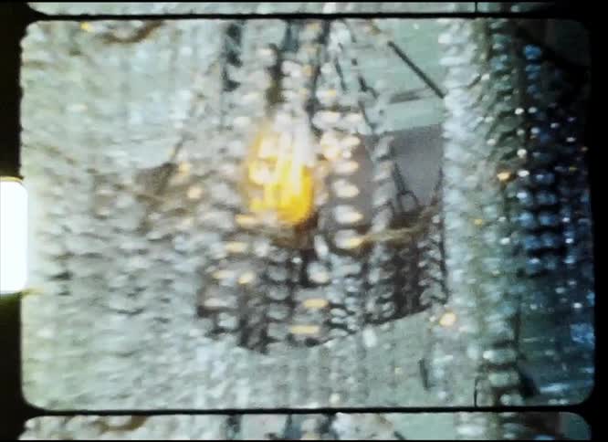 A woman reaches up touching the hanging beads on the light fixture causing them to sway