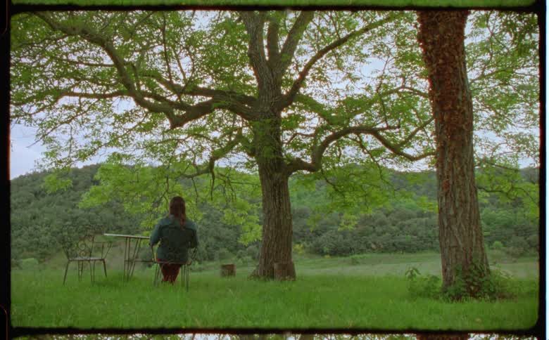 A woman sitting at a wrought iron patio set in the grass looking out at the hills