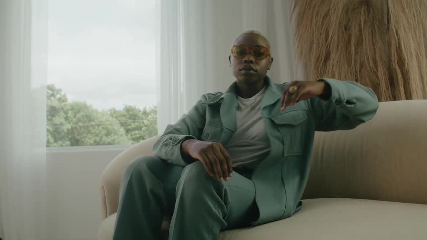 A woman wearing a pant suit and glasses is relaxing on a couch