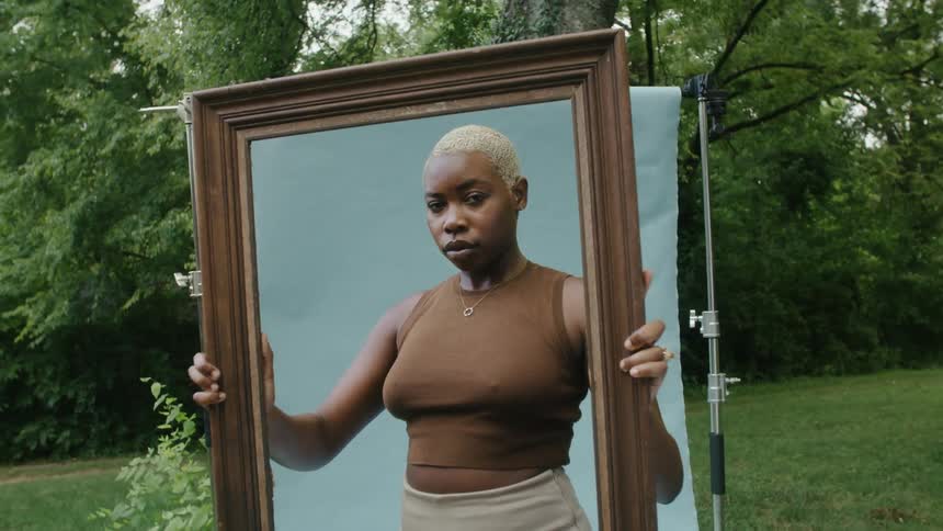 A woman is posing and holding a picture frame in front of a backdrop in a park